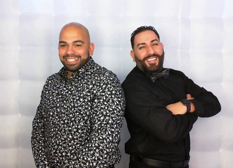 Two guests in sequinned shirts grinning in front of the lit booth backdrop