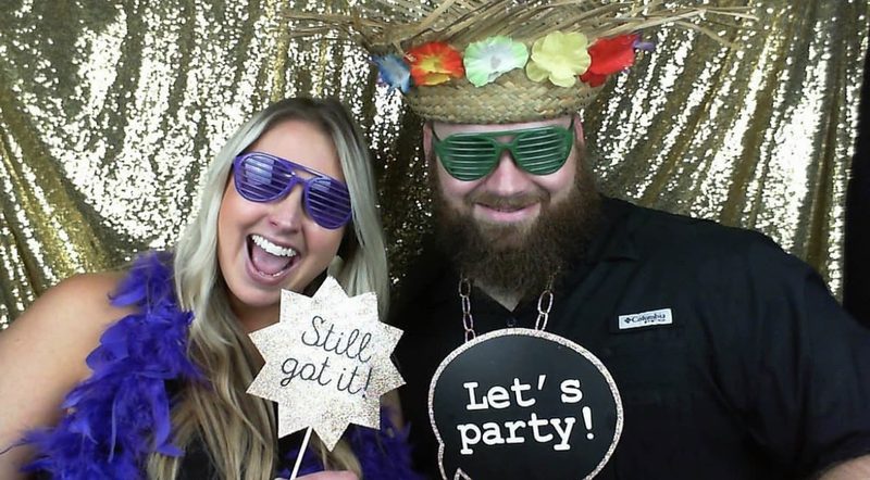 Guests in shutter shades and party hats holding celebration signs in the booth
